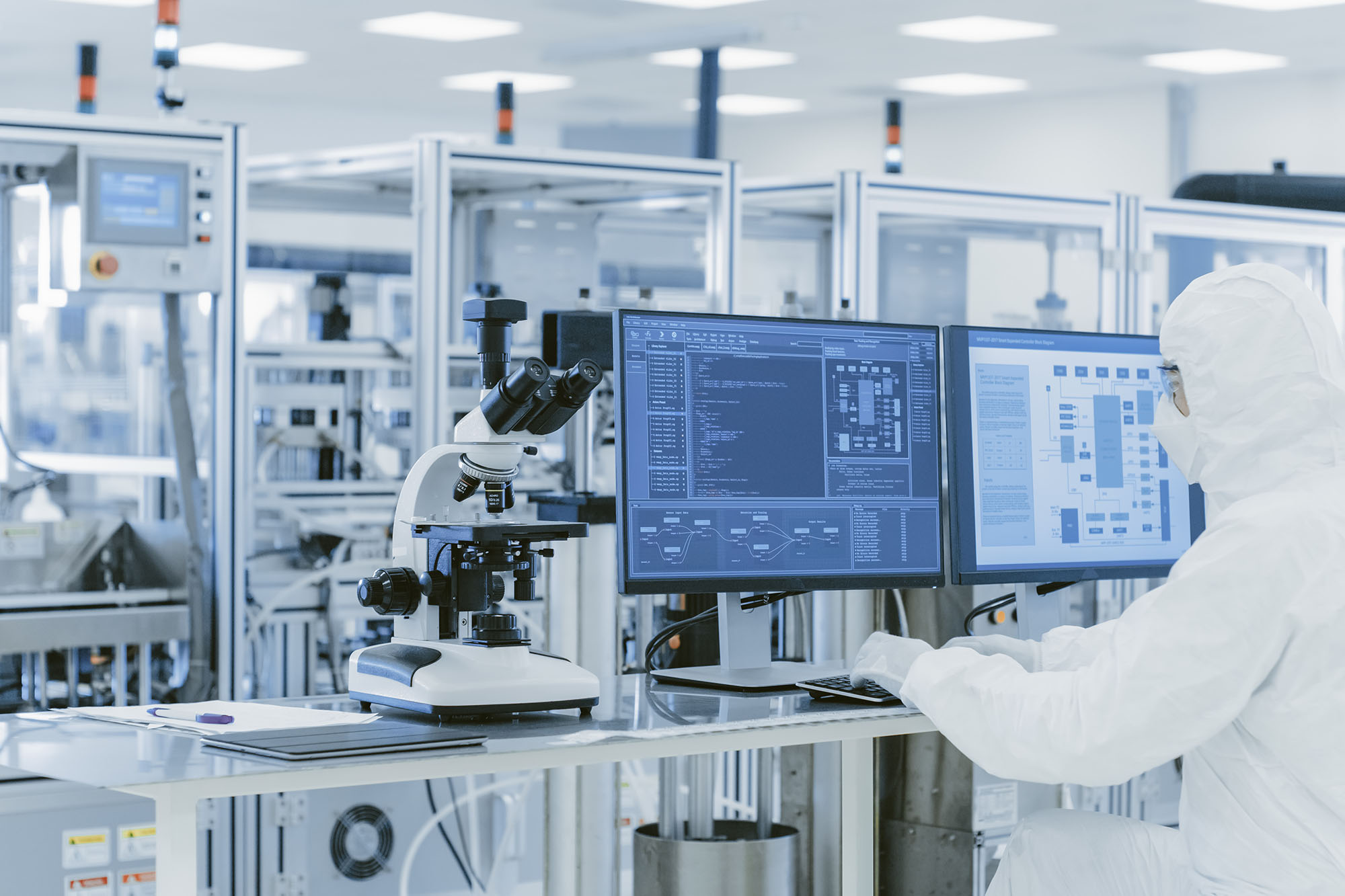 In Laboratory Over the Shoulder View of Scientist in Protective Clothes Doing Research on a Personal Computer. Modern Manufactory Producing Semiconductors and Pharmaceutical Items.