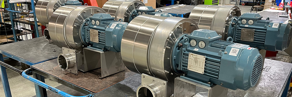 Scenario Fan Multiple custom-built industrial centrifugal fans with stainless steel housings and electric motors, arranged on a workbench in a manufacturing facility